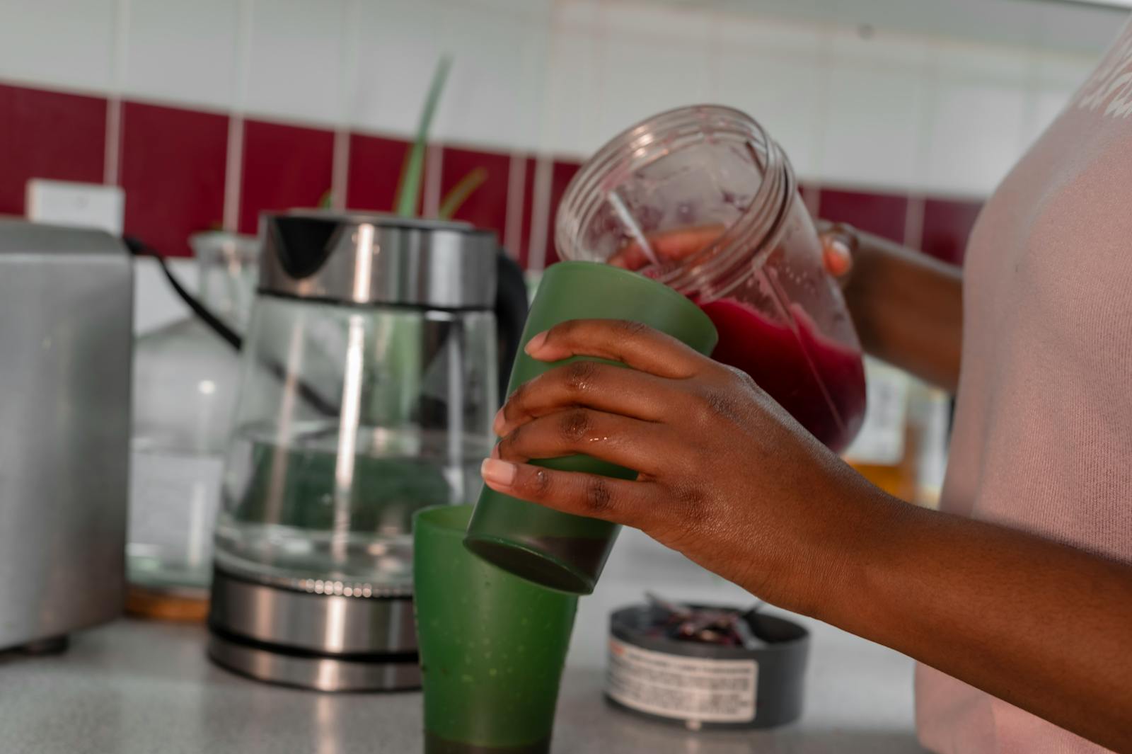 Close-up of a person pouring a healthy red smoothie into a green glass in a home kitchen.