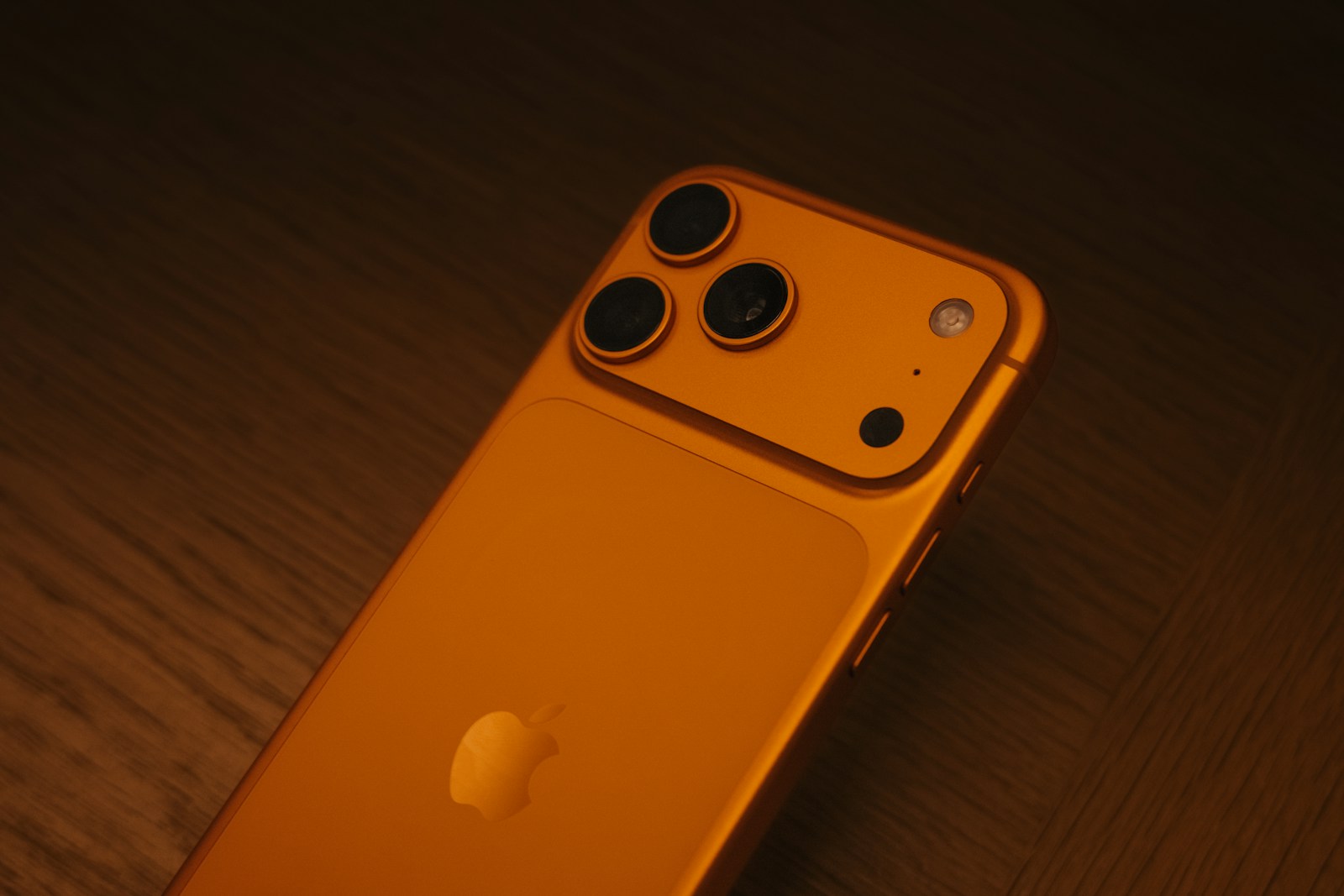 Back of an orange smartphone with three cameras.